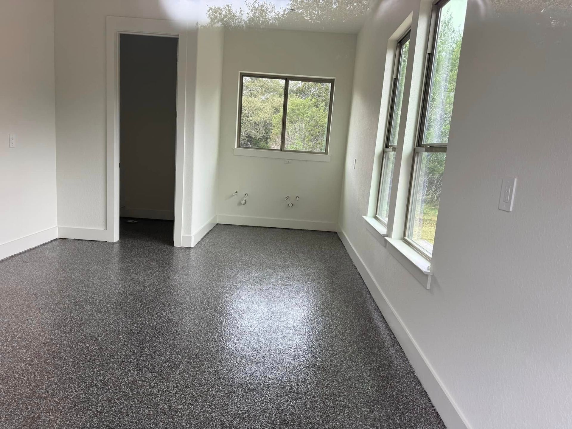 Empty room with speckled gray floor, white walls, windows, and doorway.