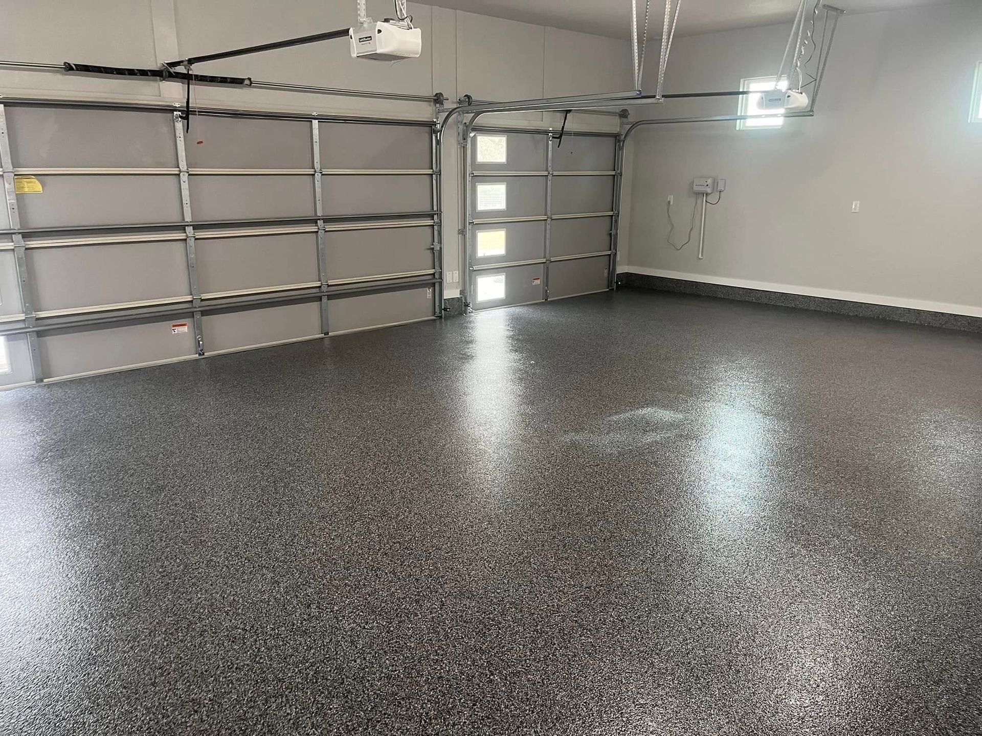 Garage with epoxy-coated floor, two gray garage doors, and overhead lighting.