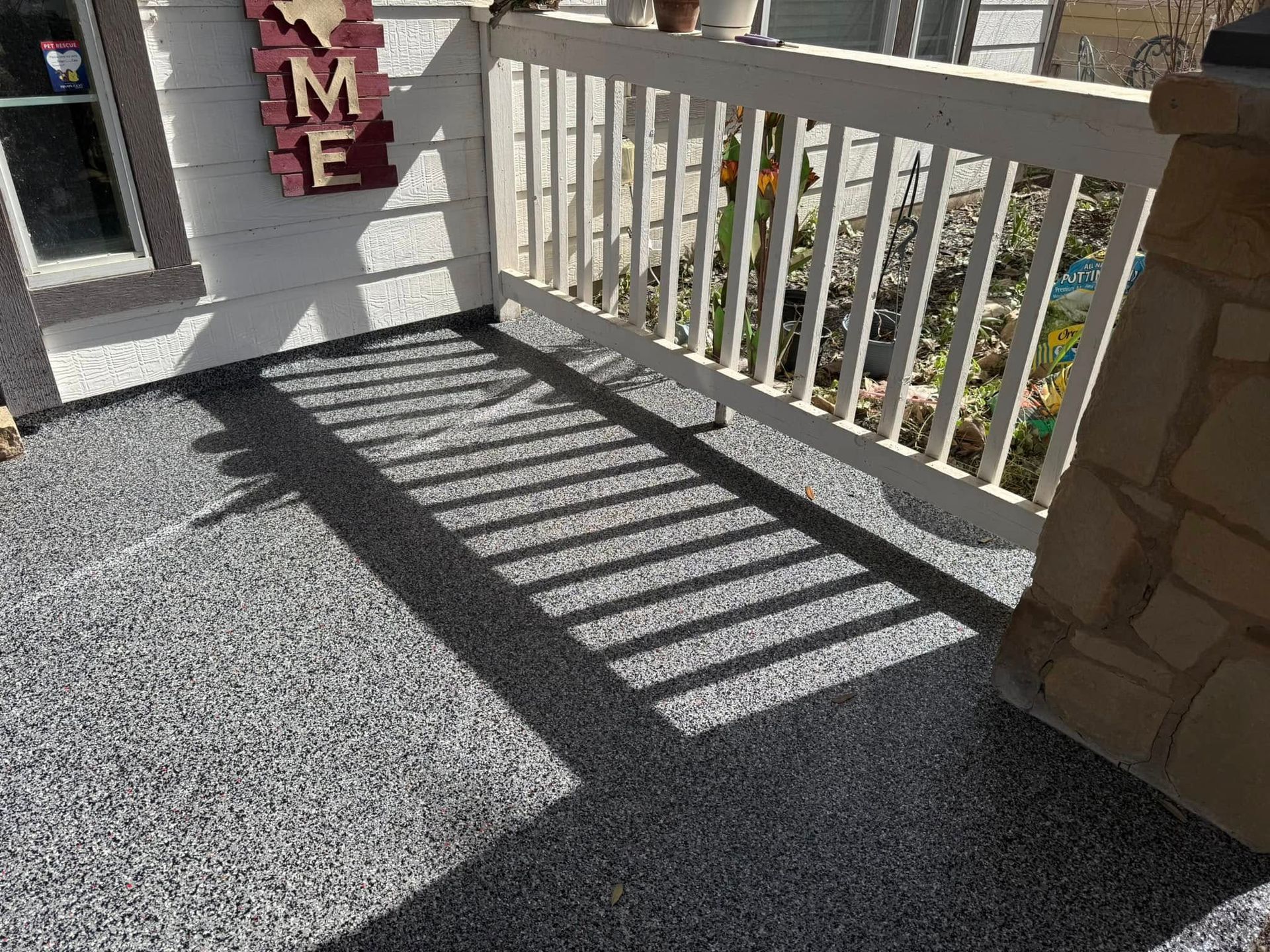 Gray speckled porch flooring with shadows from a white railing.