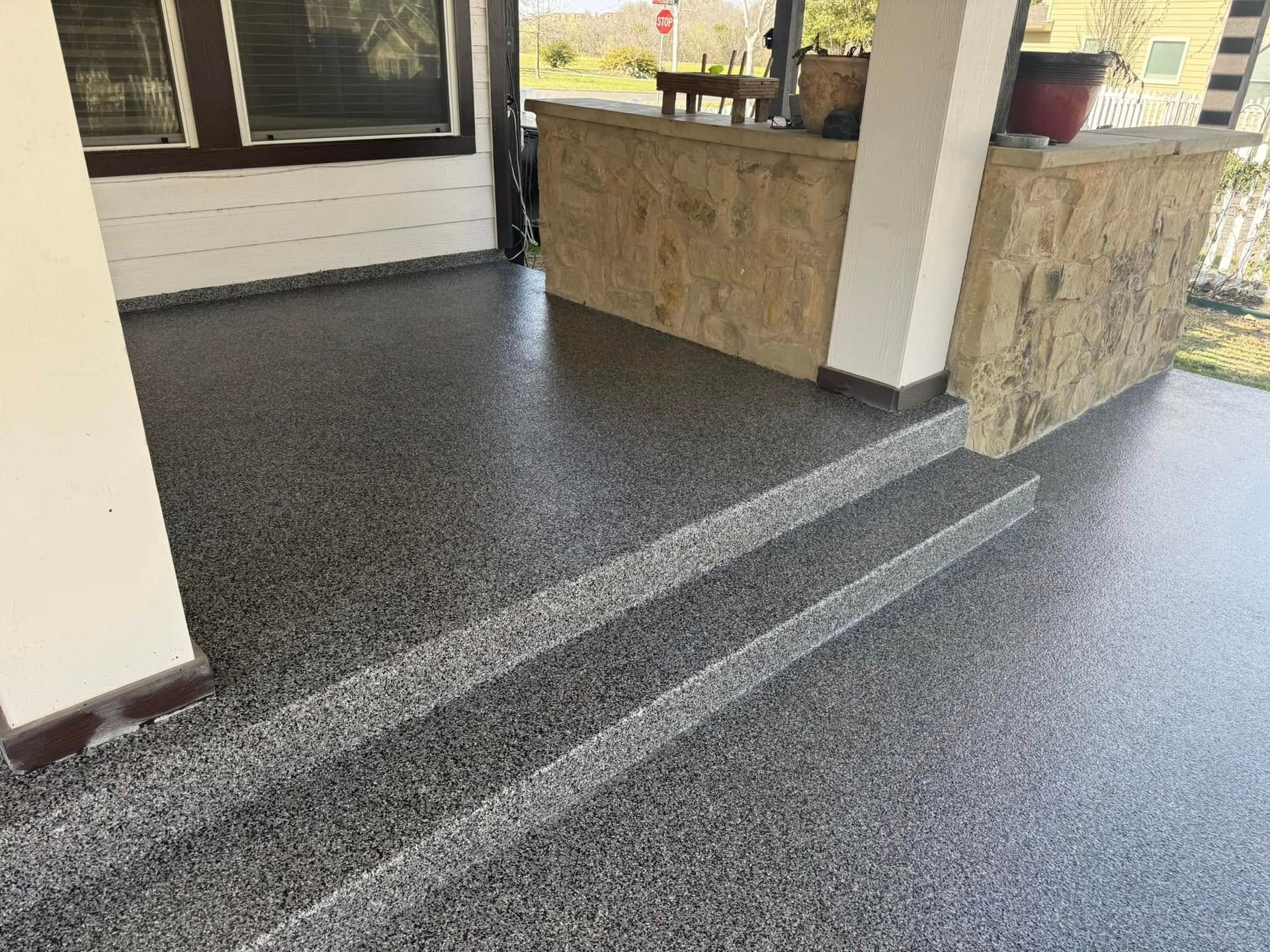 Porch with gray speckled flooring and two steps; light wood counter, a white column, and a stop sign in the background.