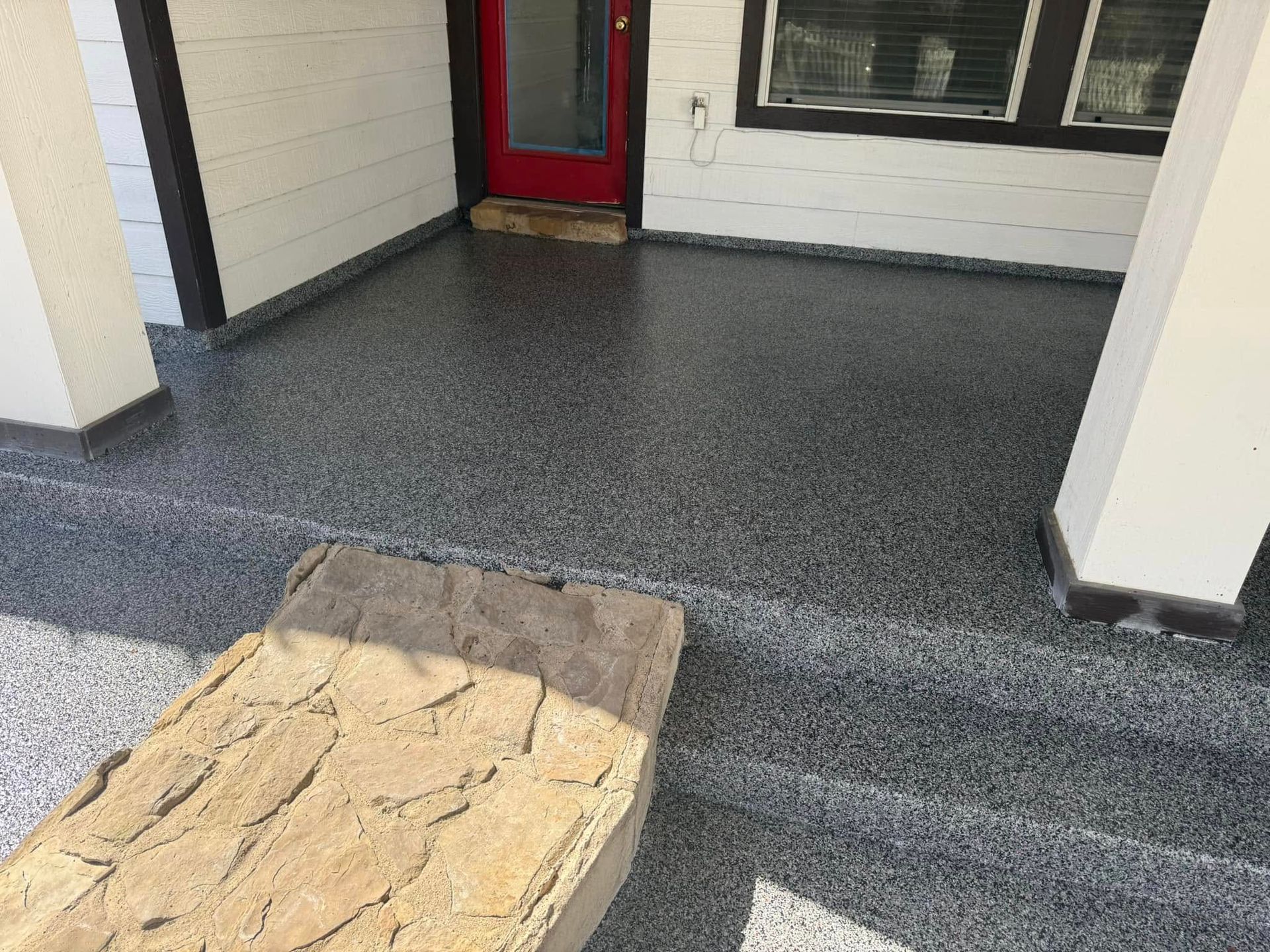 Gray speckled epoxy porch floor with a decorative mat near a red door.