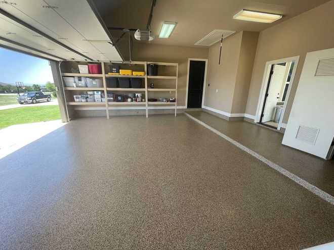 A garage interior with a shiny, speckled floor. Shelves hold storage bins; open garage door reveals a street.