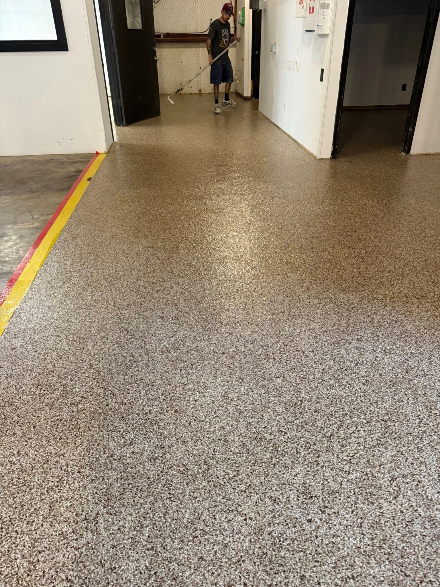 Person sweeping a speckled epoxy floor in an industrial-looking hallway.