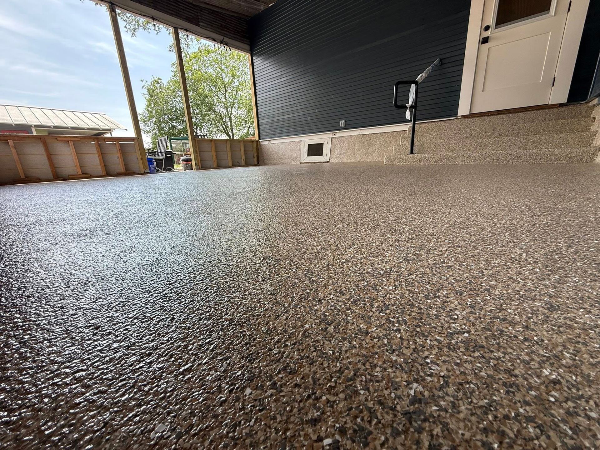 Covered porch with speckled flooring, dark siding, and a white door.