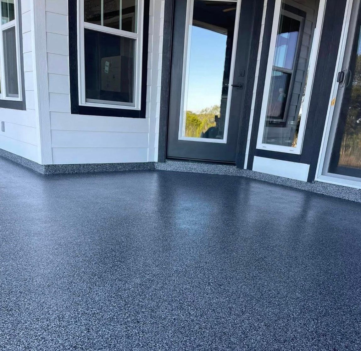 Exterior view of a house with a gray speckled epoxy floor and black-framed windows and doors.