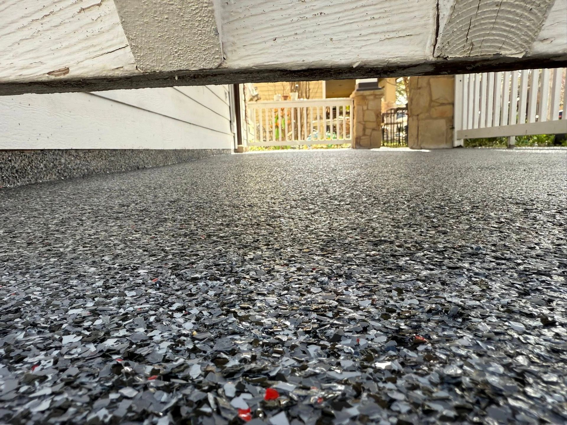 Garage floor with speckled gray coating, looking out towards a white fence.