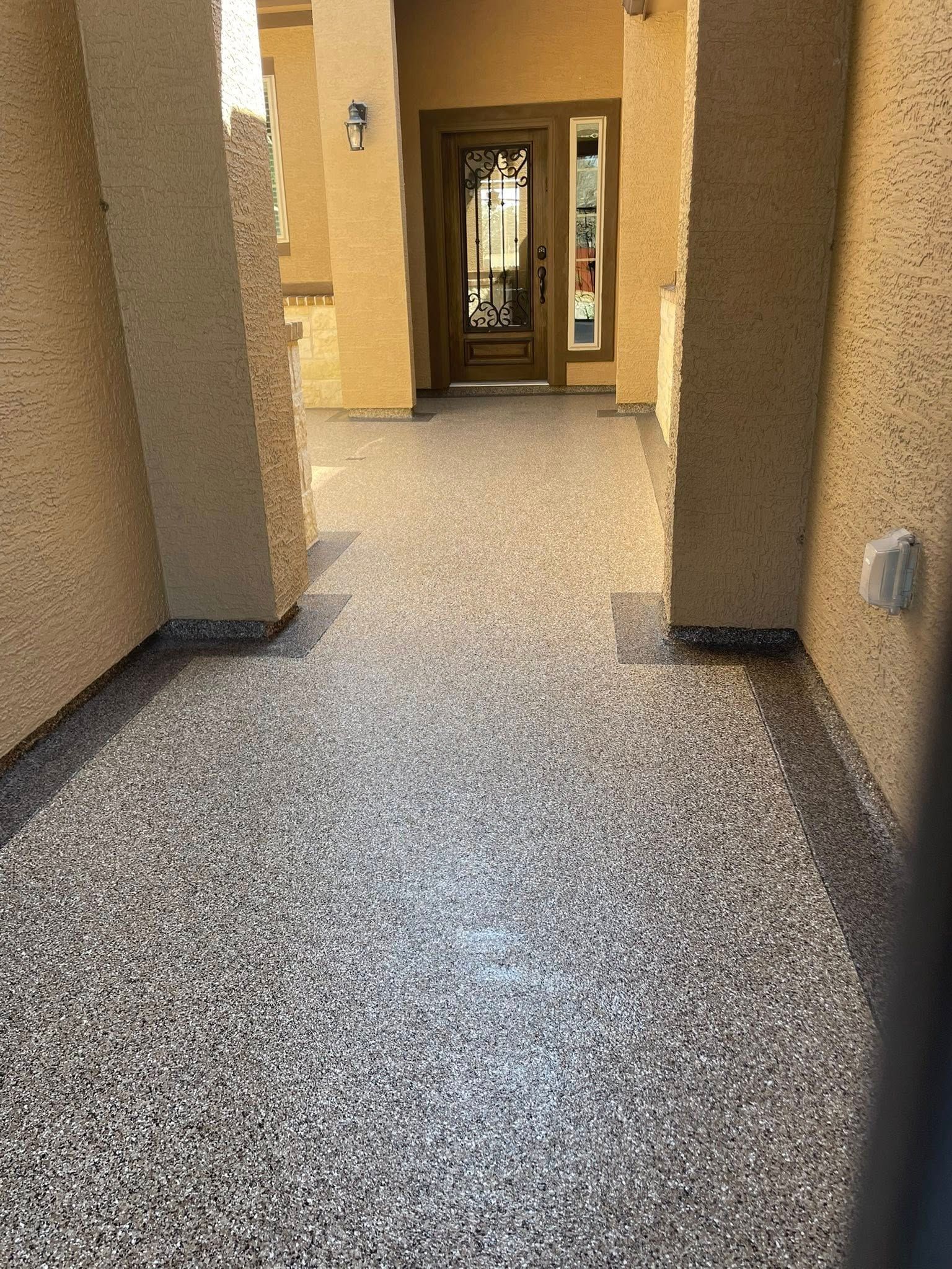 Entryway with speckled flooring, brown pillars, and a dark front door.