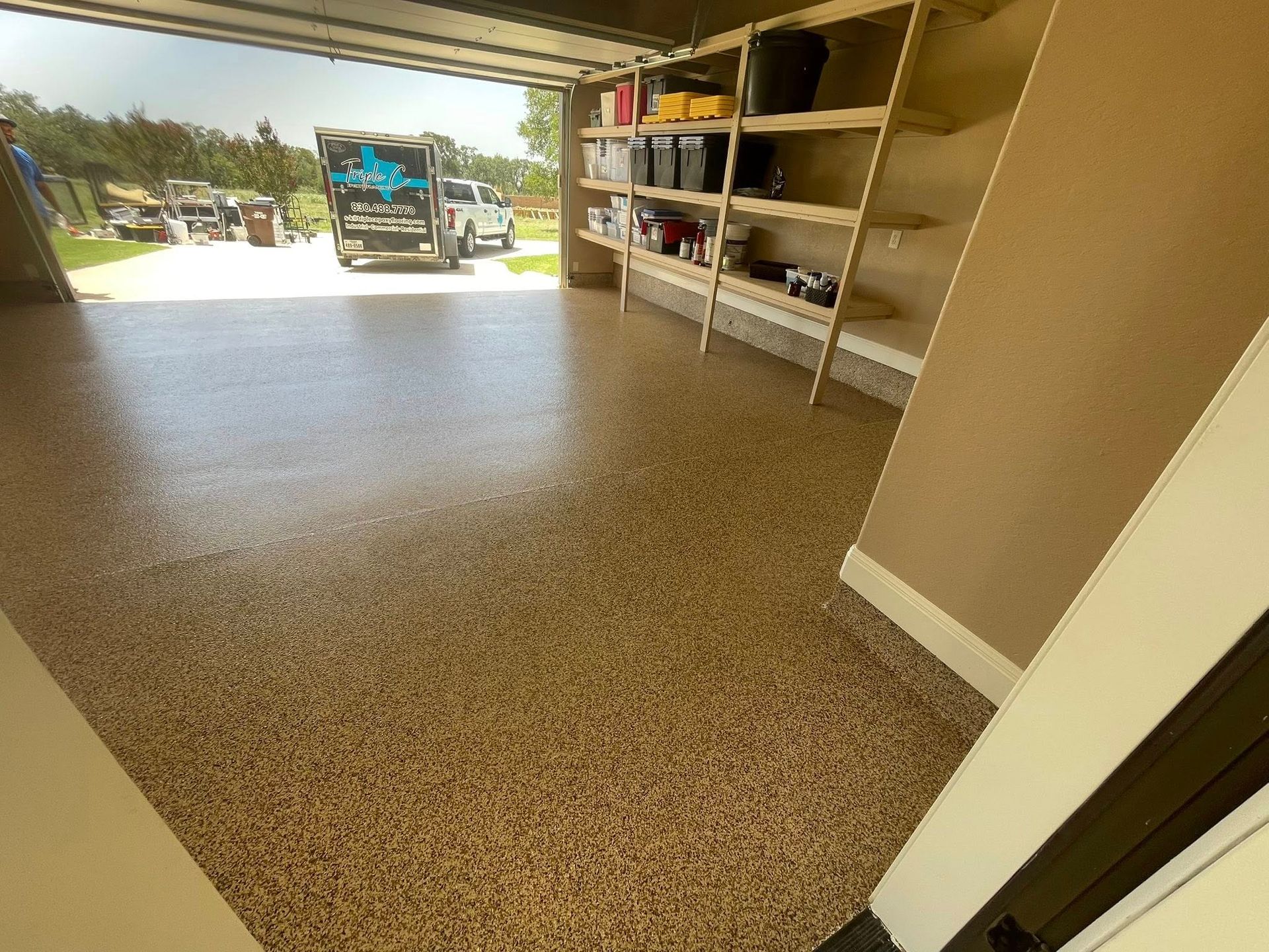 Garage interior with epoxy floor, shelves, open door to vehicles.