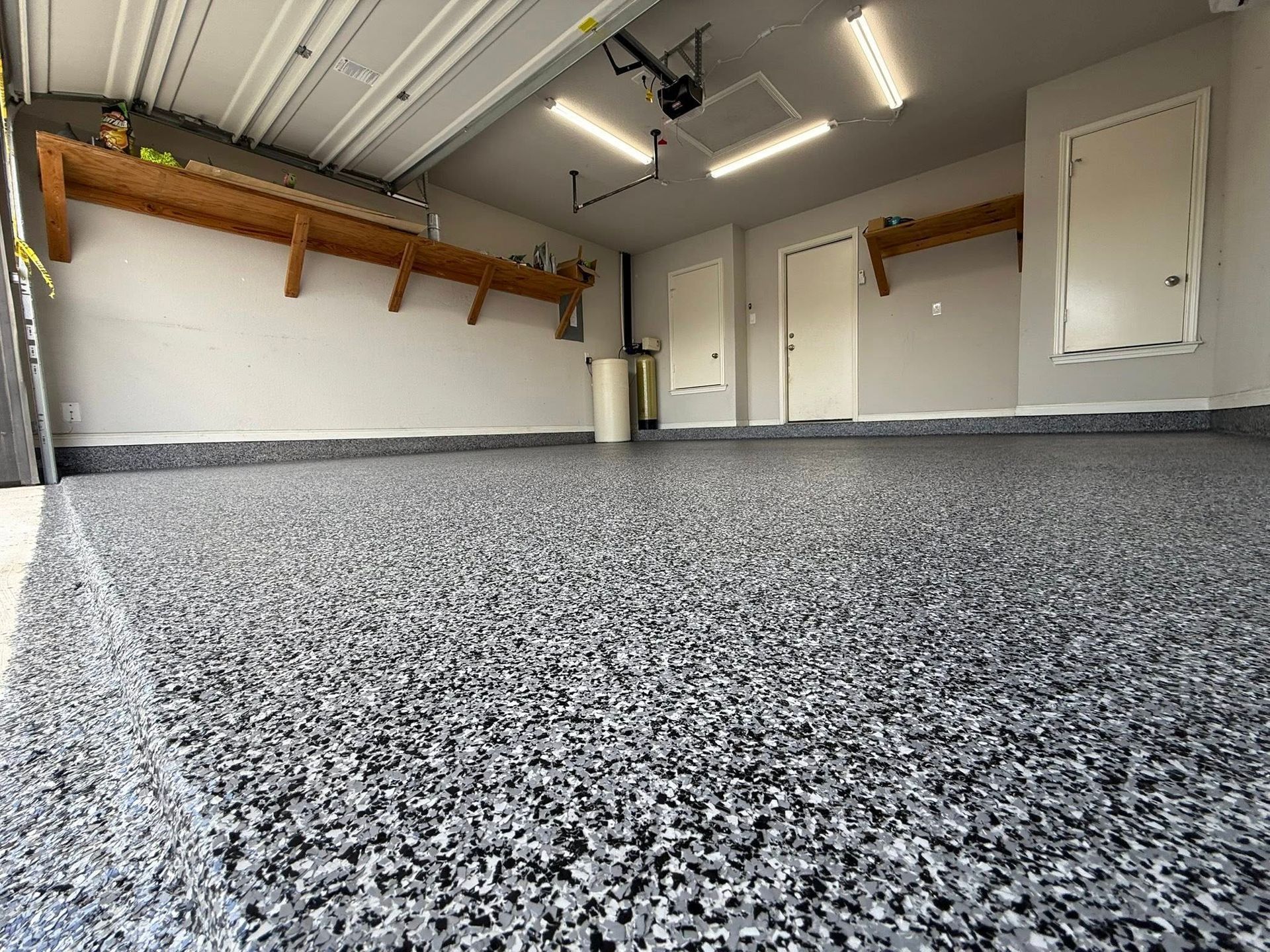 Garage interior with speckled gray epoxy floor, storage shelves, and closed doors.