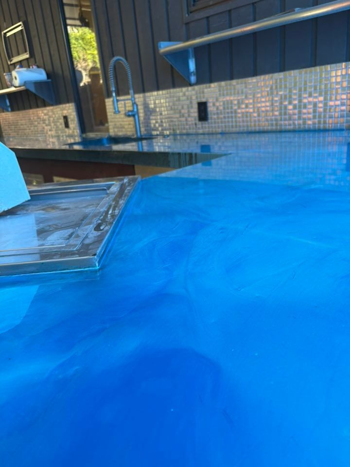 Bright blue epoxy countertop, with sink and mirrored backsplash, outdoors.