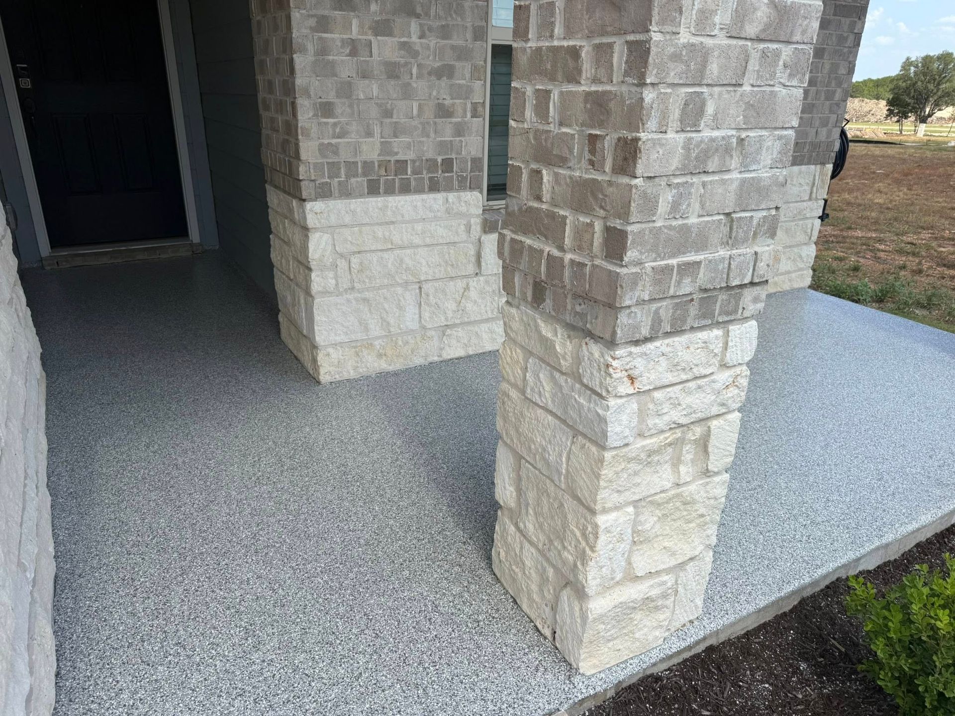 Gray speckled concrete porch with stone pillars.