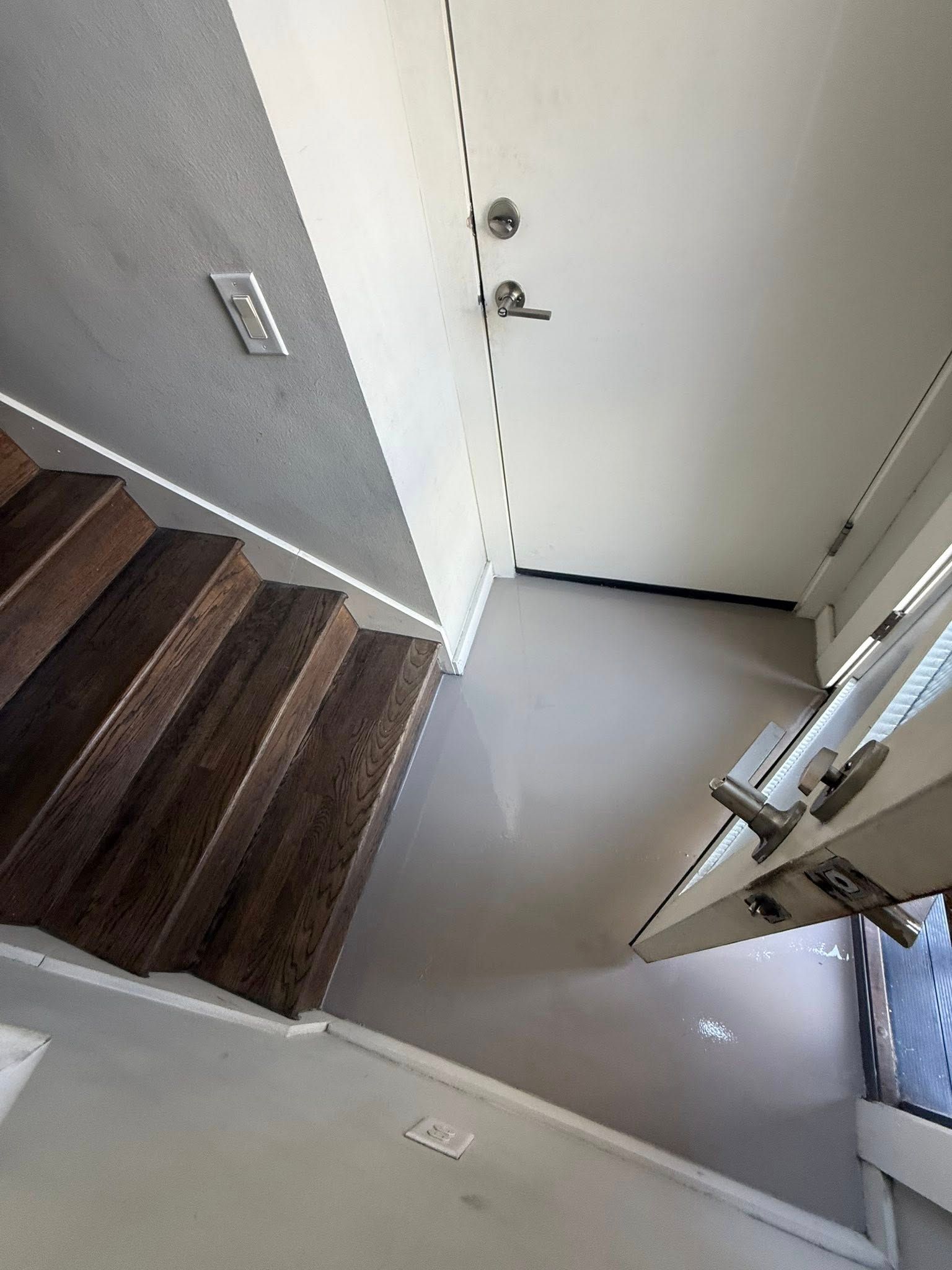 Staircase leading to a doorway, light wood steps, gray walls and floor, door ajar, bright daylight visible.