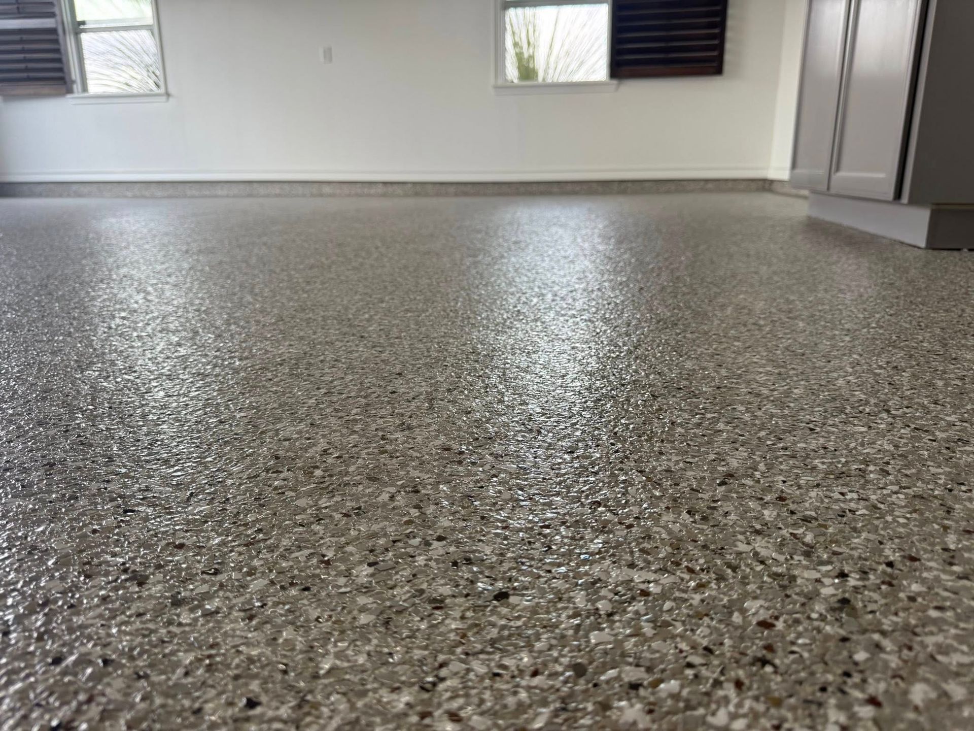 Glossy, speckled epoxy garage floor. White walls, windows with blinds.