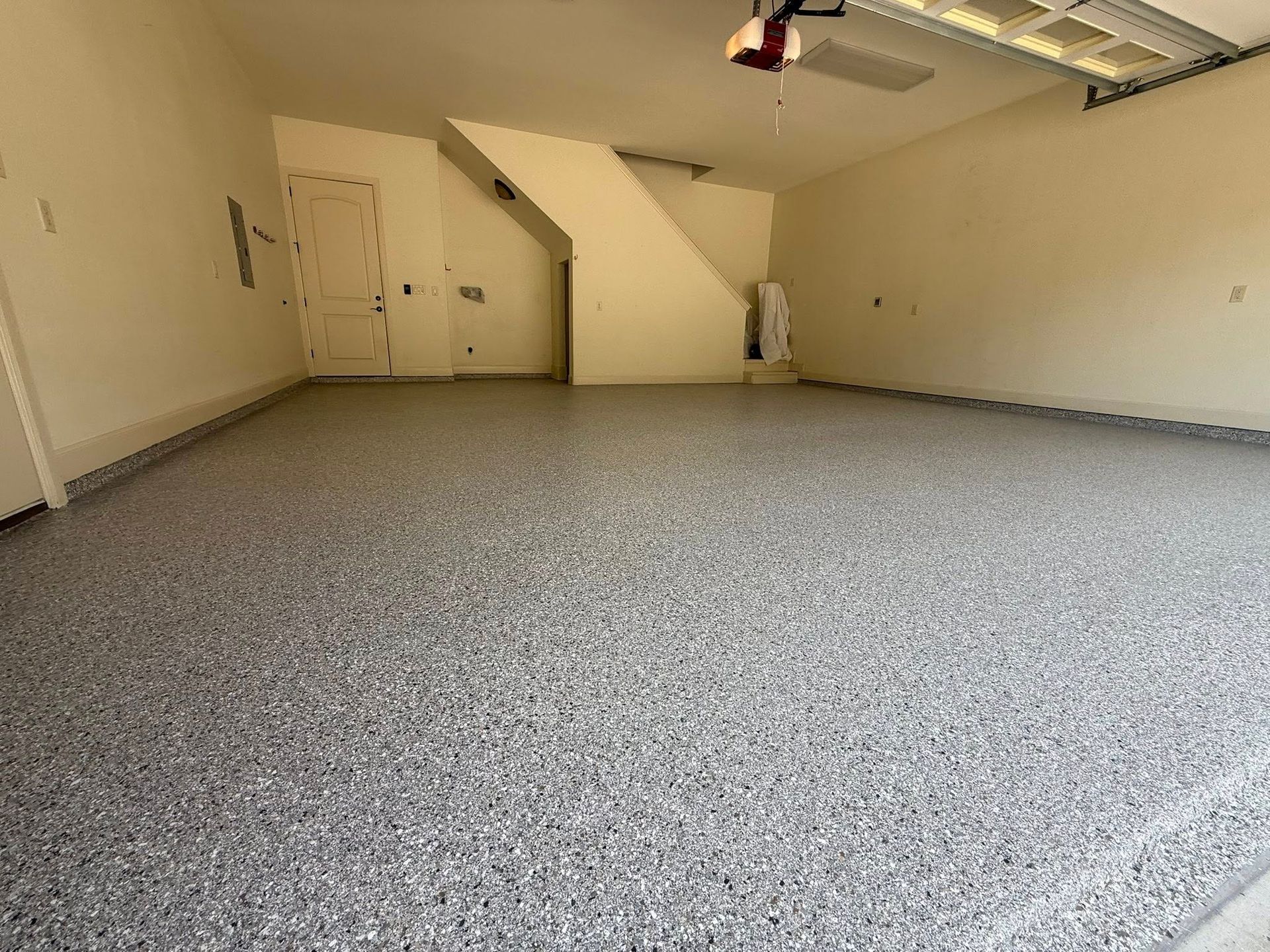 Empty garage with a gray speckled epoxy floor, white walls, and stairs in the background.