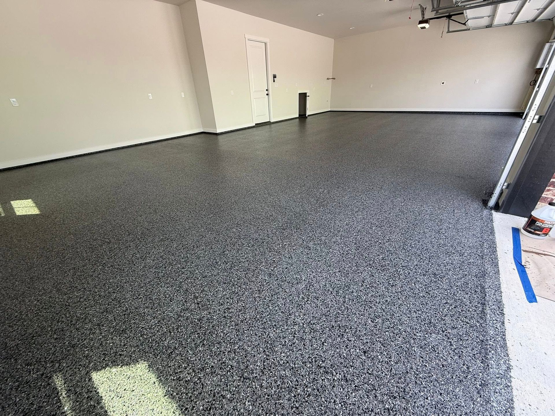 Garage with a gray speckled epoxy floor and white walls. Garage door is open.