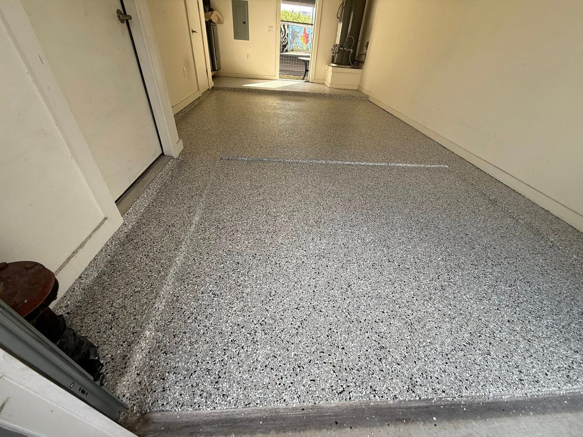 Garage floor coated with a speckled gray epoxy. A door is on the left, and another door leads outside.