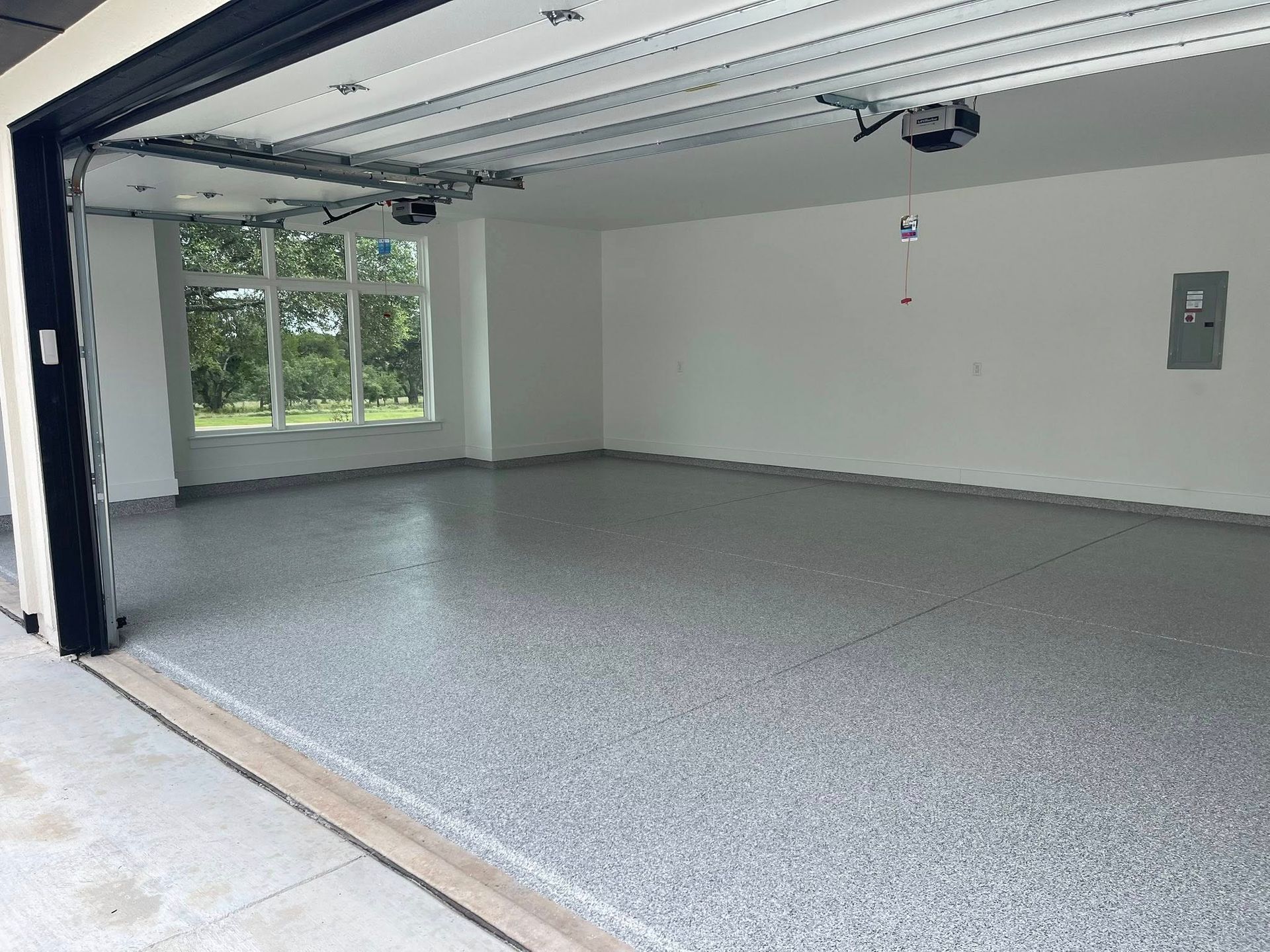 A spacious, empty garage with a gray speckled floor and a large window letting in natural light.