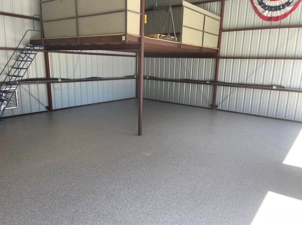 Interior view of a metal building with a concrete floor and a loft area. A red, white, and blue banner is on the wall.