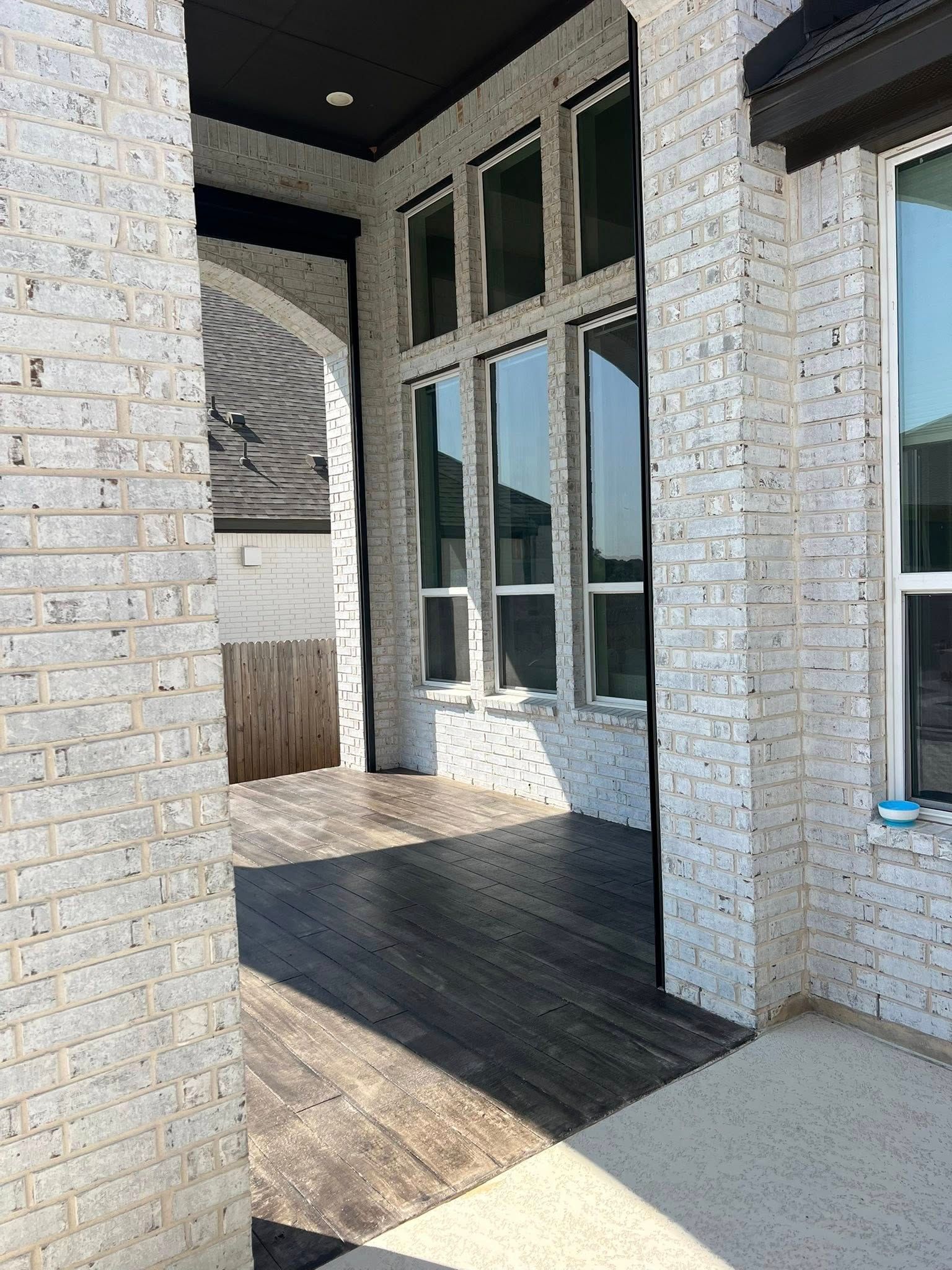 Porch with light brick columns, dark wood flooring, and tall windows.