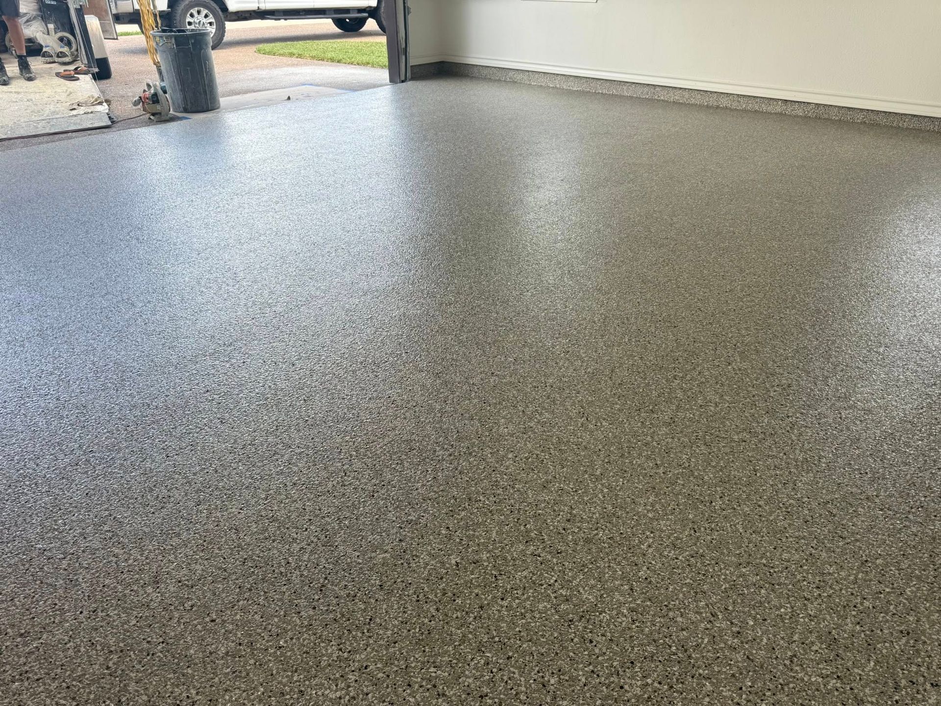 Epoxy-coated garage floor with speckled gray and brown aggregate; open garage door.