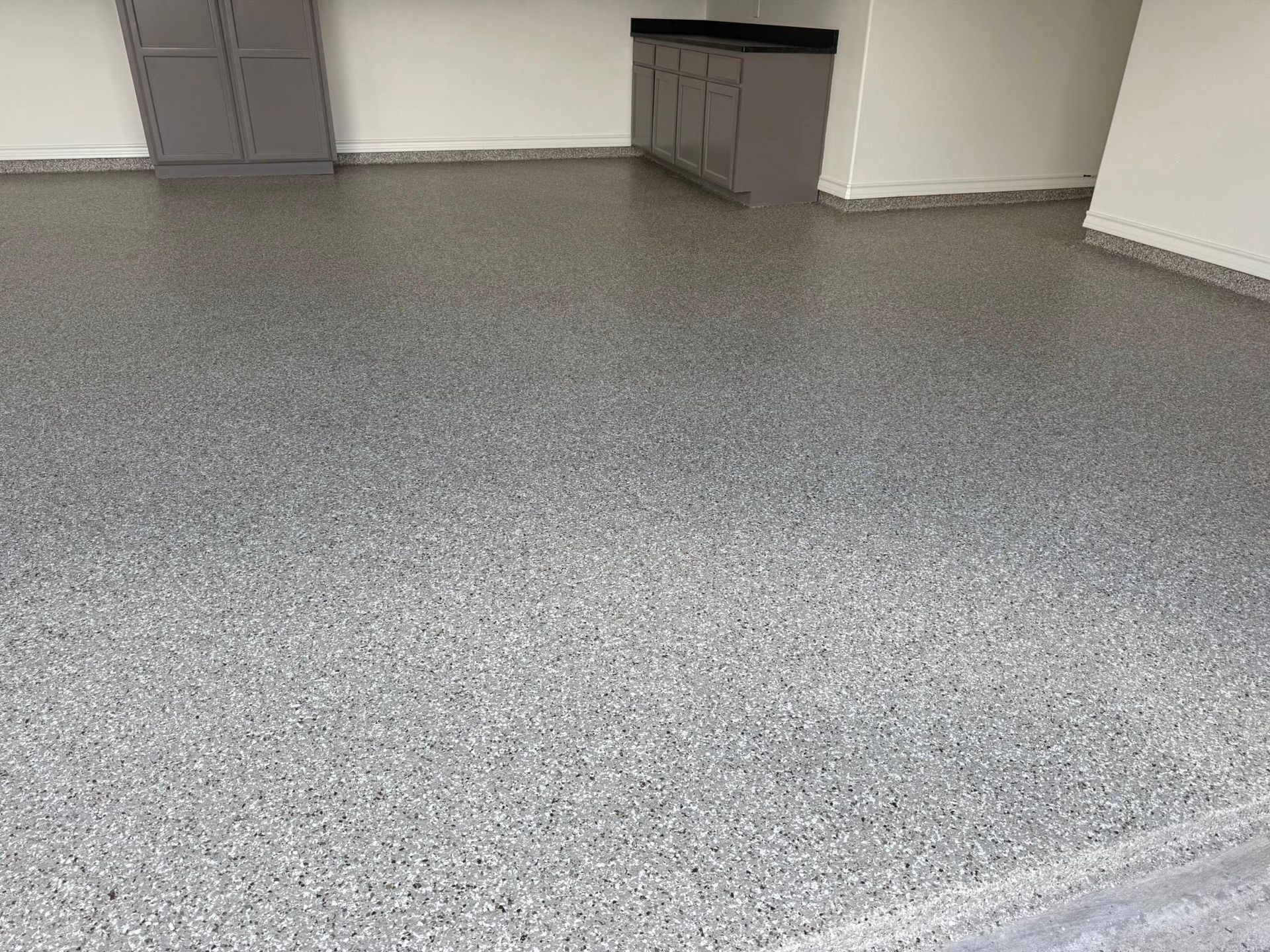 Gray speckled epoxy floor in a garage with cabinets and a storage closet.