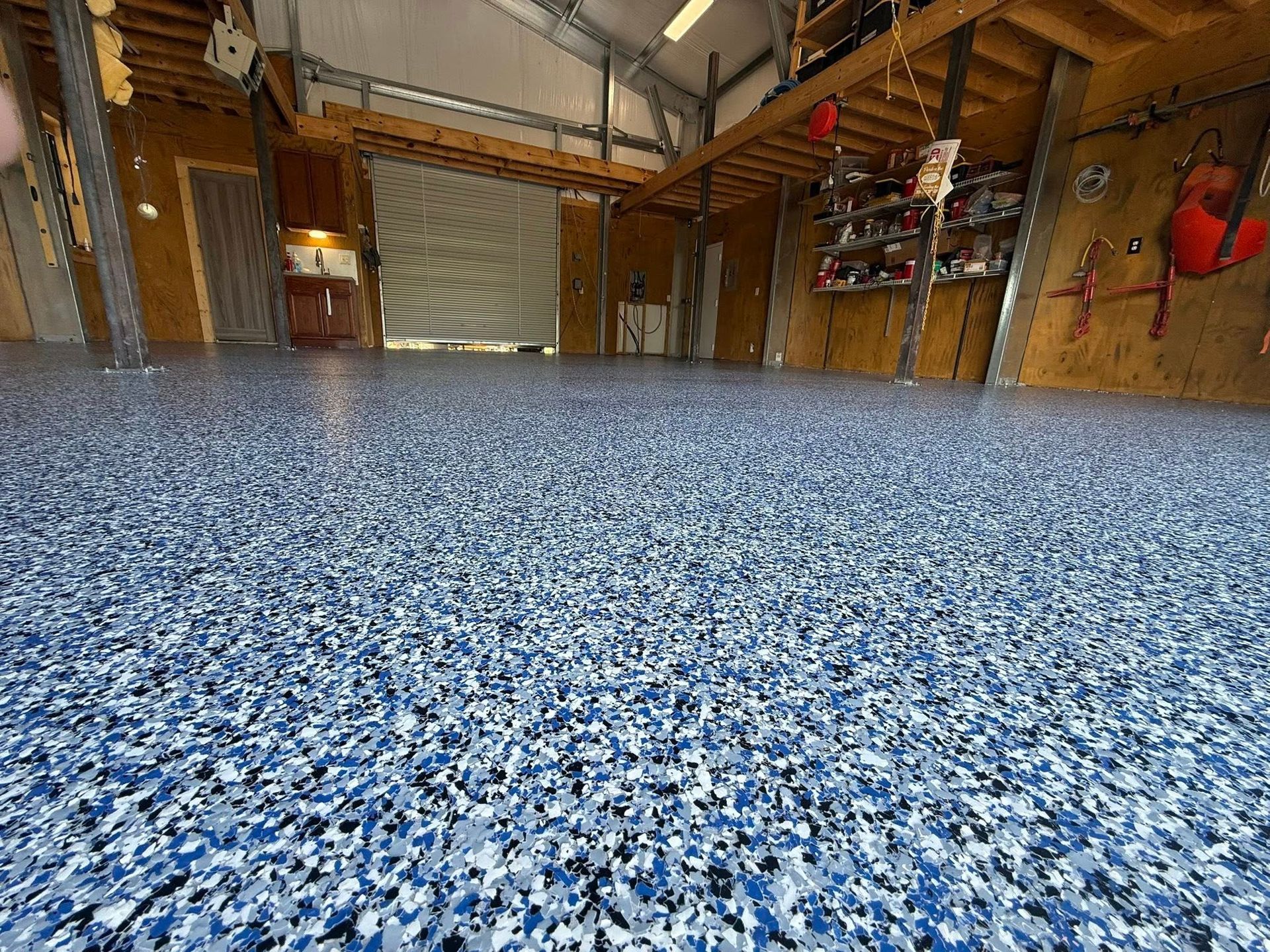 Blue and white speckled epoxy floor in a garage with a loft and open door.