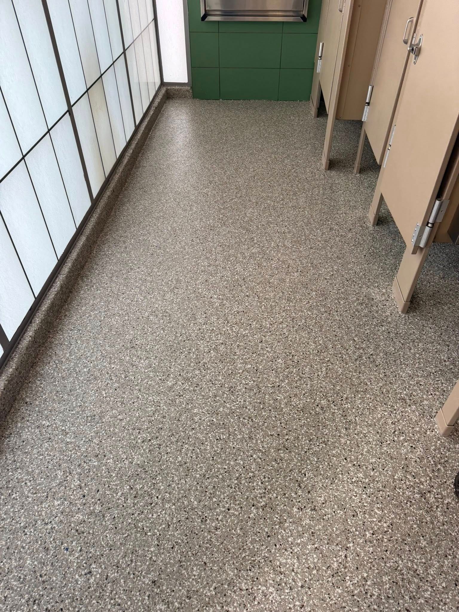 Terrazzo floor in a public restroom. Beige stalls on the right, frosted glass wall on the left, and green cabinet in the background.