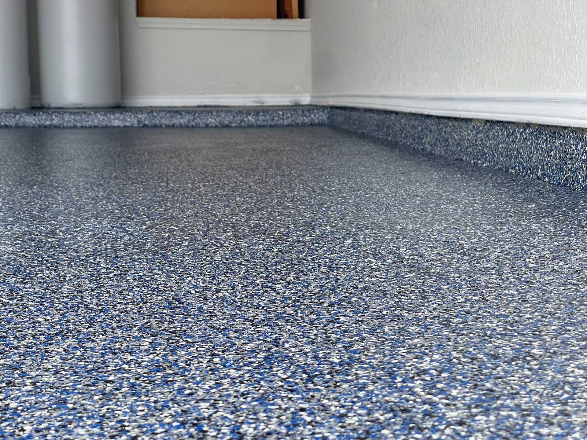 Epoxy garage floor with blue, white, and gray chips, next to a white wall and storage area.