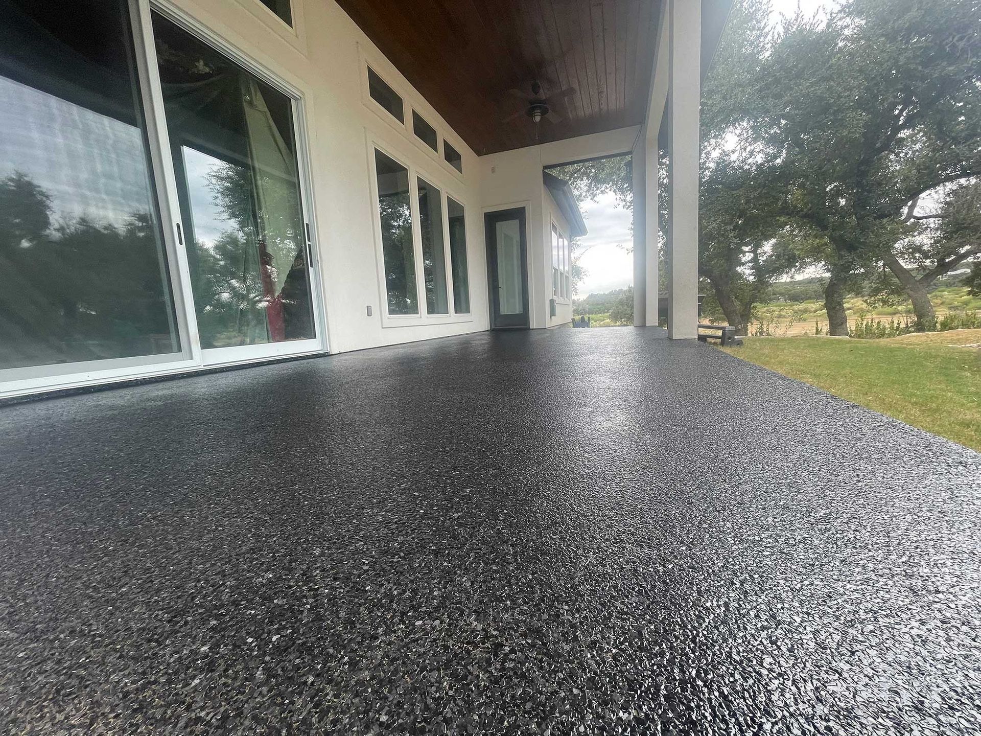 Black speckled concrete patio with large windows, covered porch, and grassy yard.