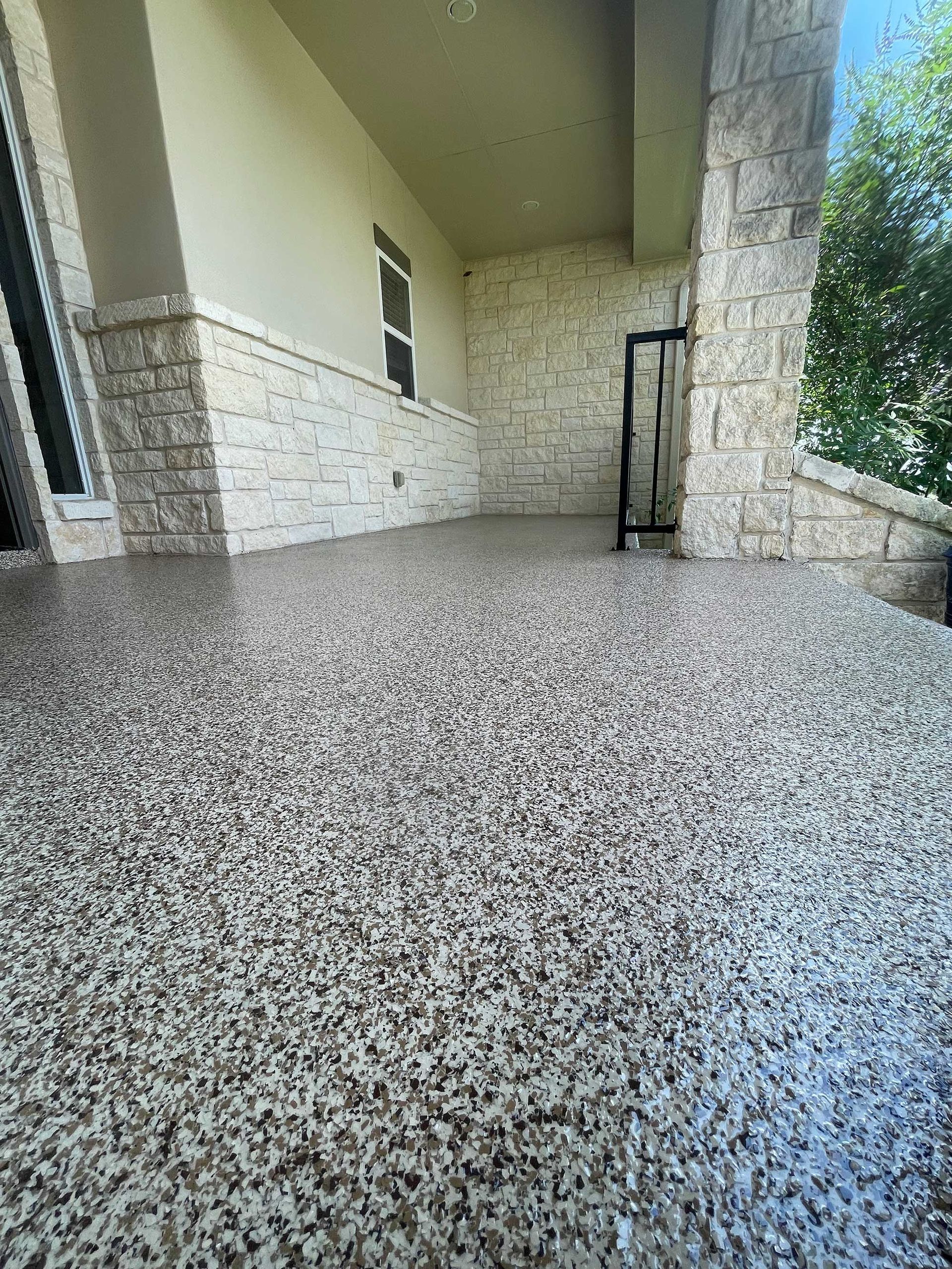 Covered porch with speckled flooring; light-colored stone walls and columns.