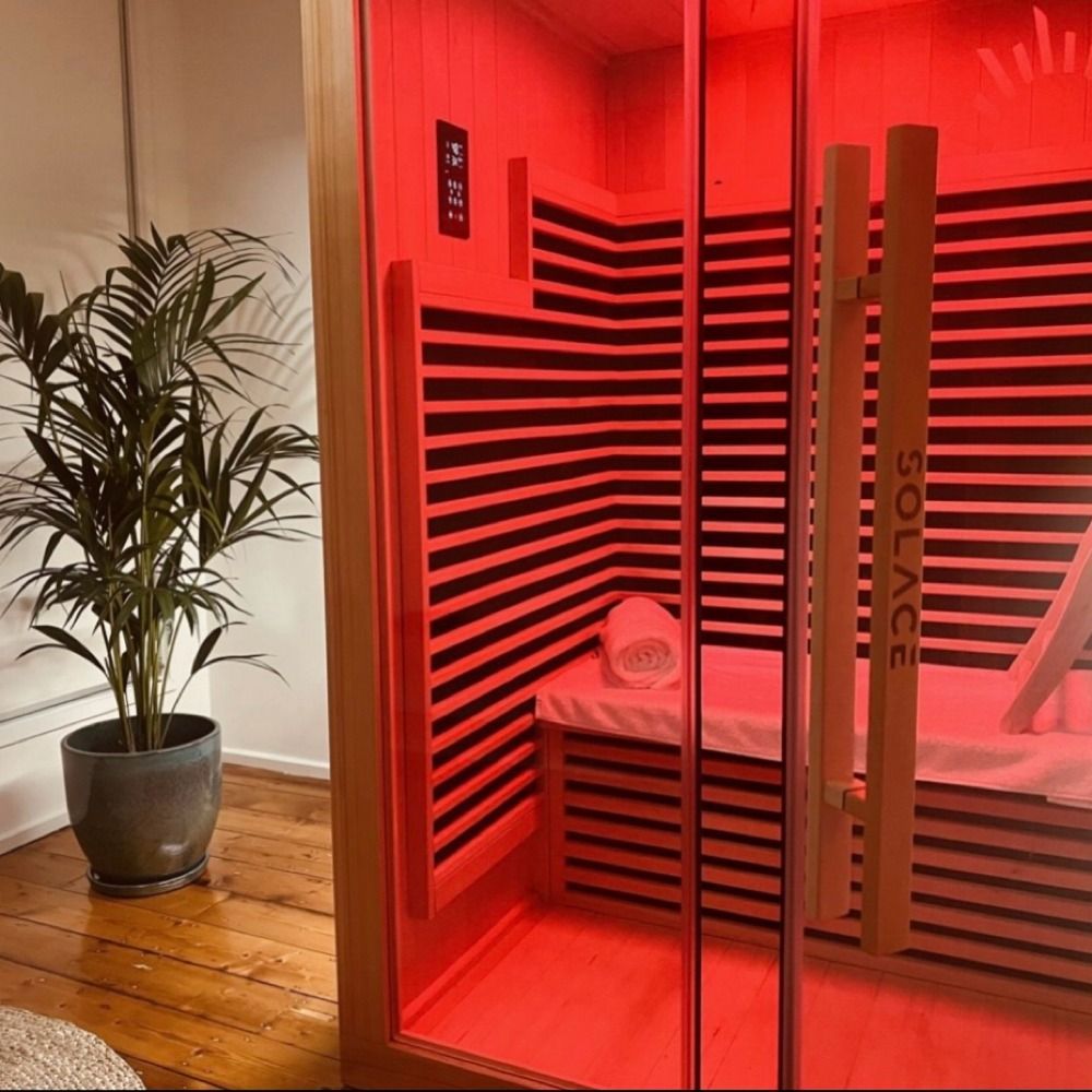Red-lit sauna booth with striped walls next to a potted plant on a wooden floor