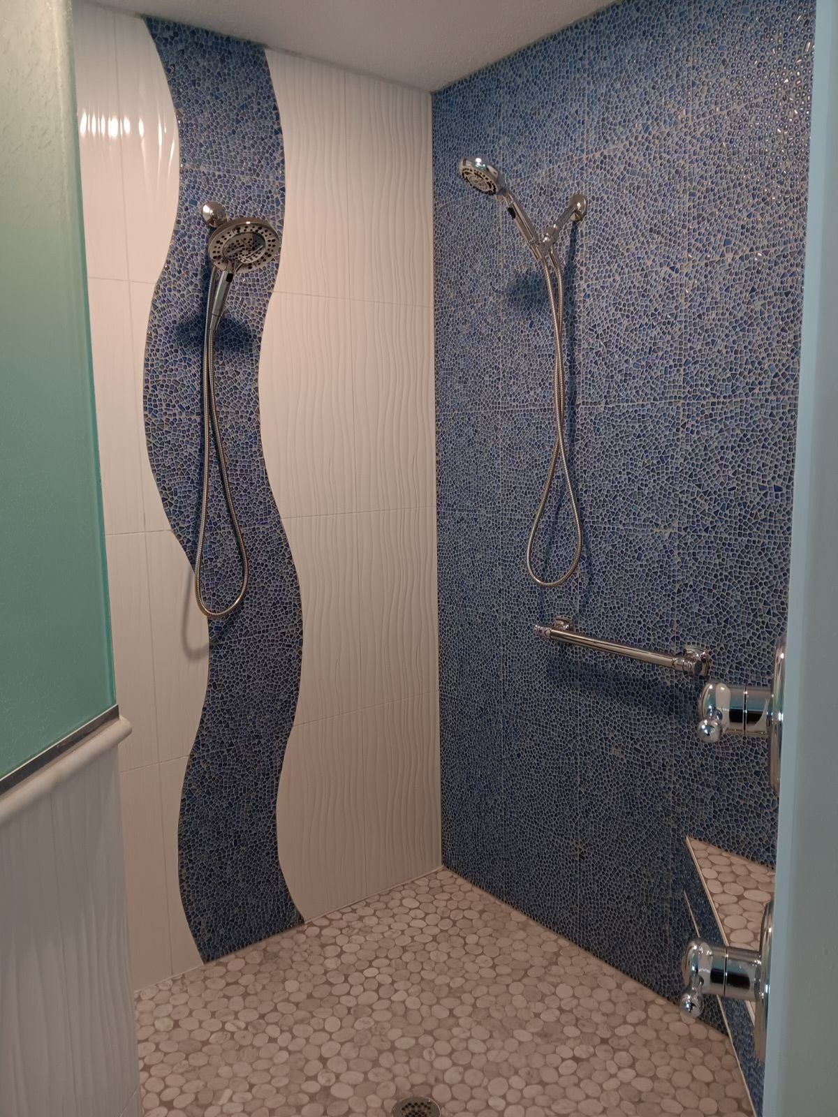 Small tiled shower stall with blue mosaic walls and a showerhead.