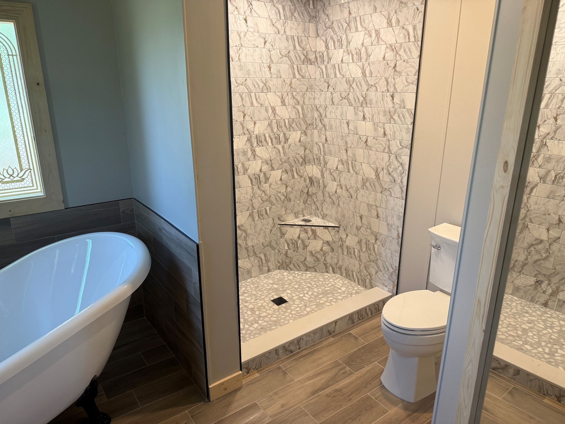 Bathroom with a white bathtub, walk-in shower, and toilet in a tiled, neutral-toned interior
