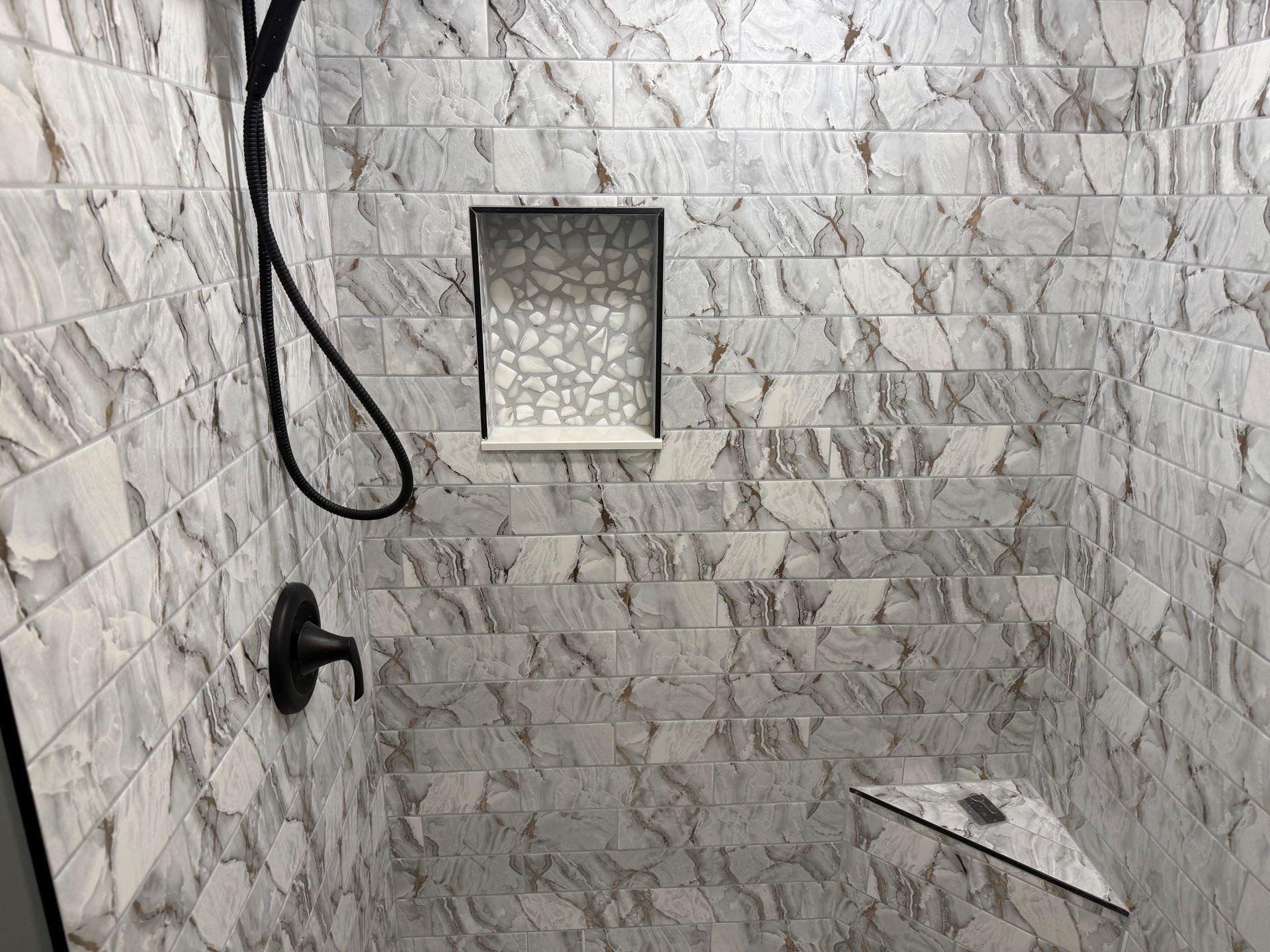 Empty tiled shower with black showerhead and small recessed shelf.