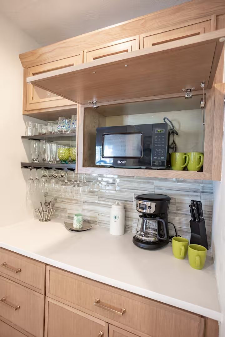 Kitchen counter with coffee maker, mugs, microwave, and glassware in light wood cabinets