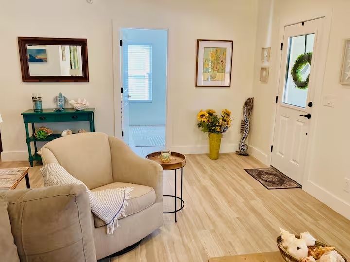 Bright living room with beige armchair, green console table, flowers, and a white front door with wreath