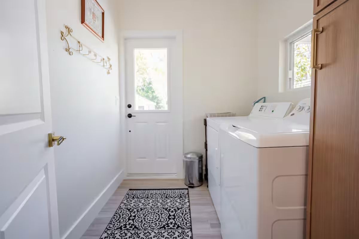 Bright laundry room with washer and dryer, patterned rug, and a door with frosted glass.