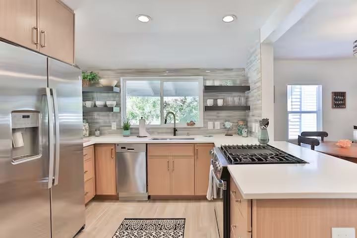 Modern kitchen with stainless steel appliances, white countertops, and a window over the sink.