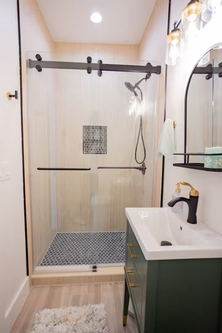 Modern bathroom with walk-in shower, green vanity, round mirror, and patterned floor mat