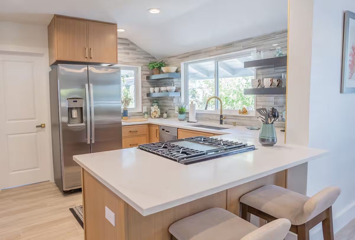 Bright modern kitchen with stainless steel fridge, island cooktop, and large windows