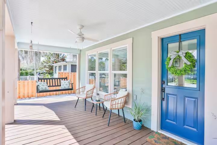 Covered porch with blue front door, white chairs, and a wooden swing overlooking a neighborhood street