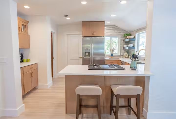 Bright modern kitchen with island, two stools, stainless appliances, and a window view