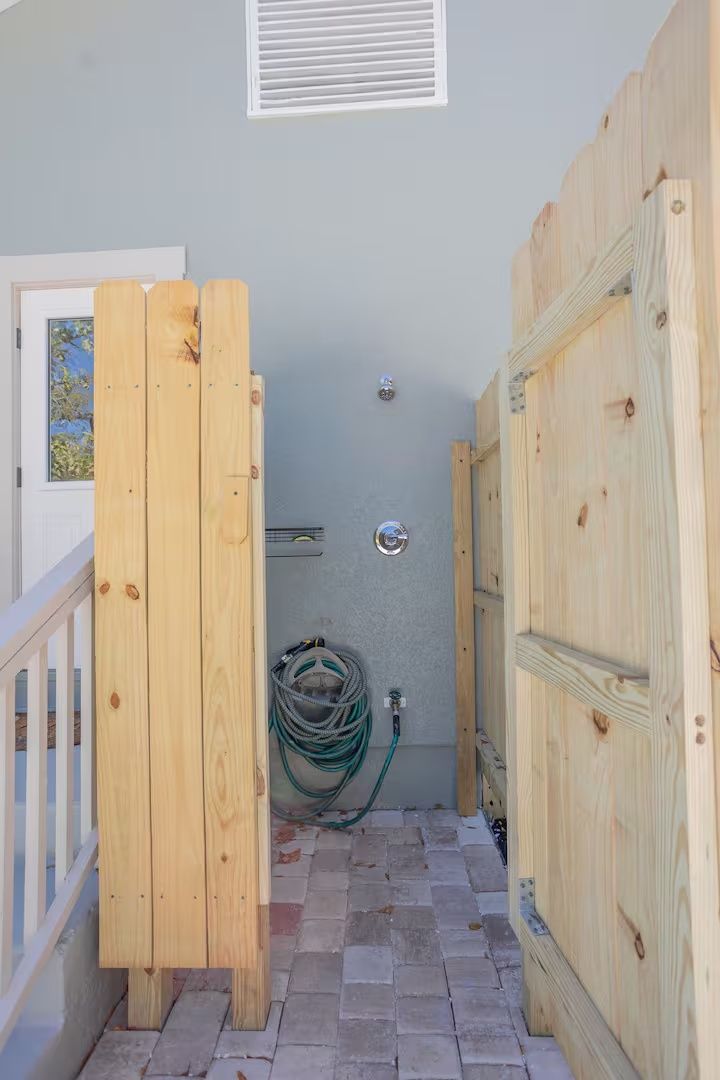 Narrow hallway with plywood partitions, brick floor, and coiled hose against a gray wall