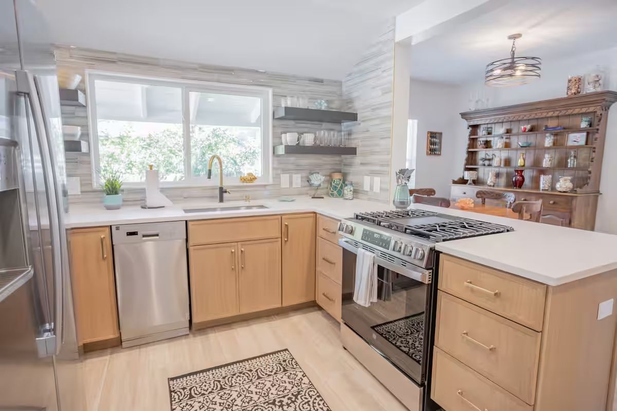 Bright modern kitchen with wood cabinets, stainless appliances, large window, and white countertops