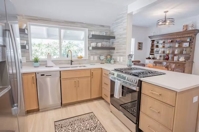 Bright modern kitchen with wood cabinets, stainless appliances, large window, and white countertops