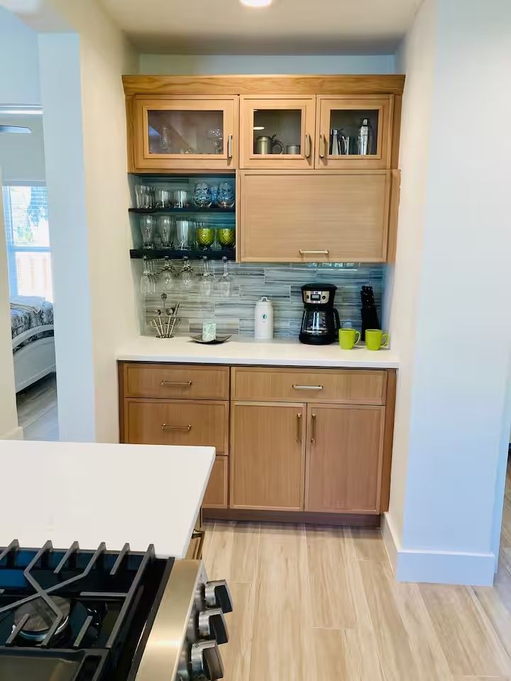 Small kitchen alcove with wooden cabinets, glassware shelves, coffee maker, and countertop near a gas stove