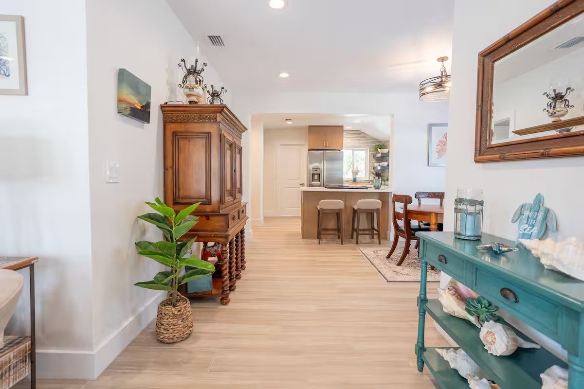 Bright hallway with light wood floors, plants, wooden cabinet, and teal console in a modern home
