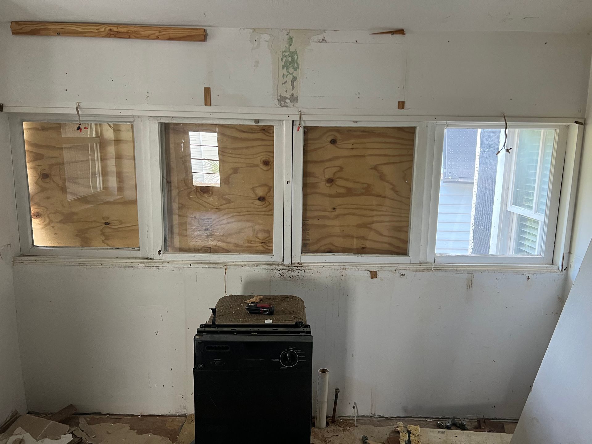 Room with four boarded-up windows, white walls, and a black stove centered below them.