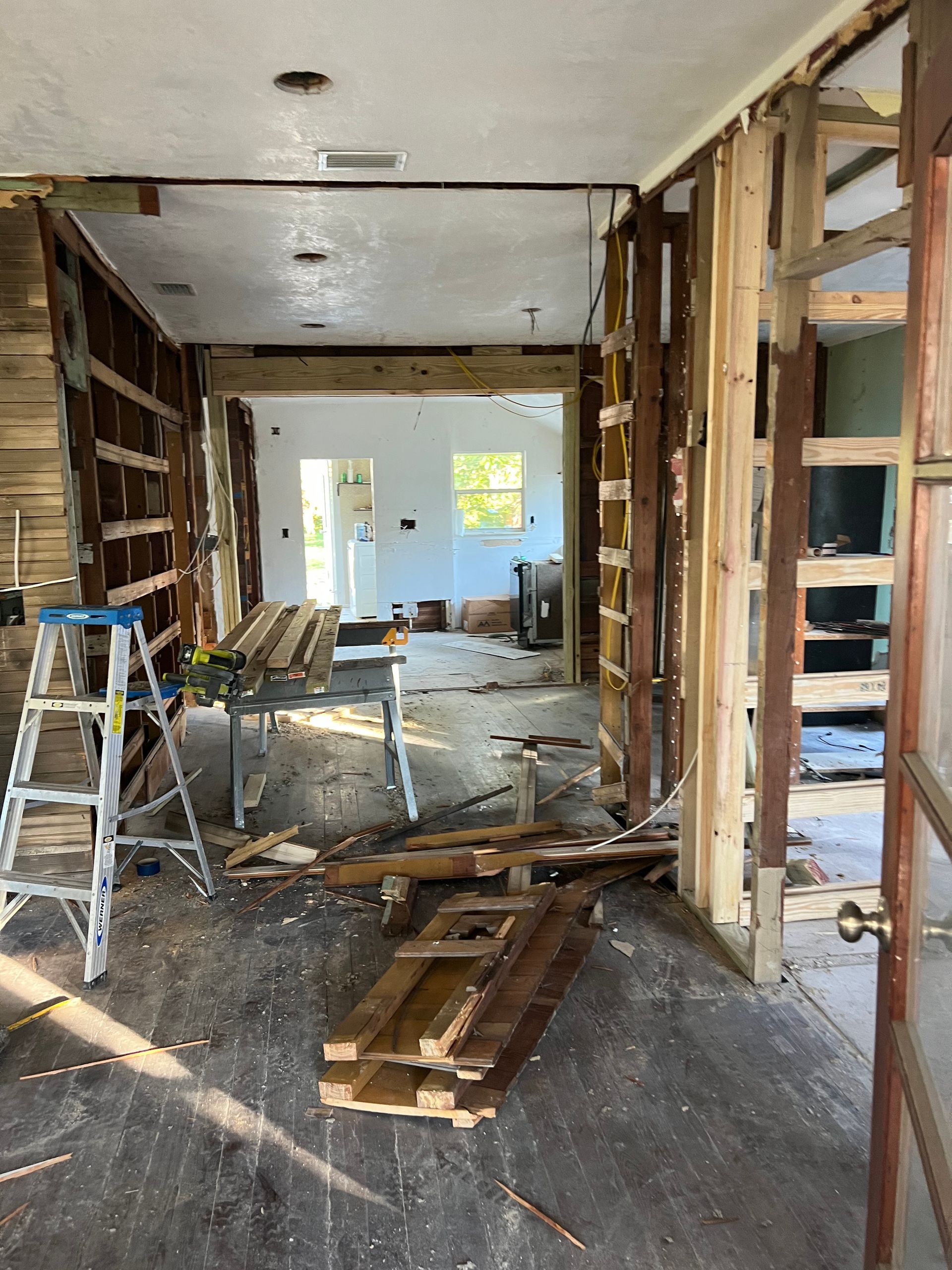 Partially demolished interior room with exposed studs, debris on the floor, and a ladder and chairs inside