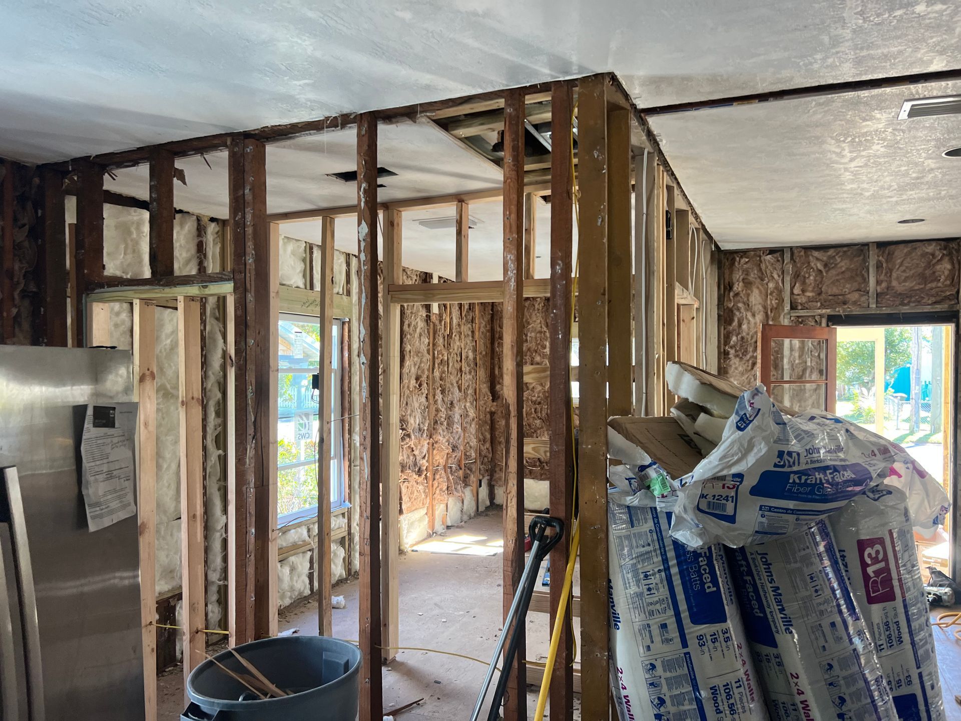 Interior of a house under renovation, with exposed wall studs, insulation bags, and unfinished drywall.